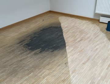 Abgenutzten Parkettboden auffrischen: Mosaikparkett in englischem Verband mit einem schwarzen großen Flec0, der zum Teil abgeschliffenen ist