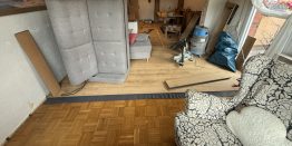 Designbelag wird auf alten Parkettboden verlegt in möbliertem Wohnzimmer
