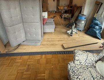 Designbelag wird auf alten Parkettboden verlegt in möbliertem Wohnzimmer